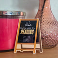Pink candle, vase with peach flowers, and small sign on a wooden surface.