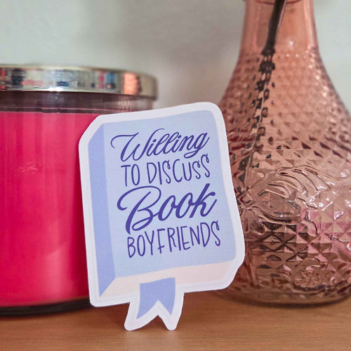 Sticker with 'Willing to discuss book boyfriends' text next to a pink candle and decorative vase.