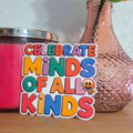 Colorful sticker with 'Celebrate Minds of All Kinds' text next to a pink candle and vase on a wooden surface.