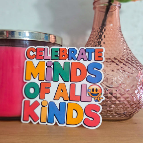 Colorful sticker with 'Celebrate Minds of All Kinds' text next to a pink candle and vase on a wooden surface.