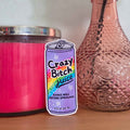 Sticker with 'Crazy Bitch Juice' design on a surface with a pink candle and textured vase.