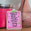 Pink card with text on a wooden surface next to a pink candle and vase with flowers.