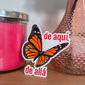 Butterfly sticker with text next to a pink candle and vase on a wooden surface