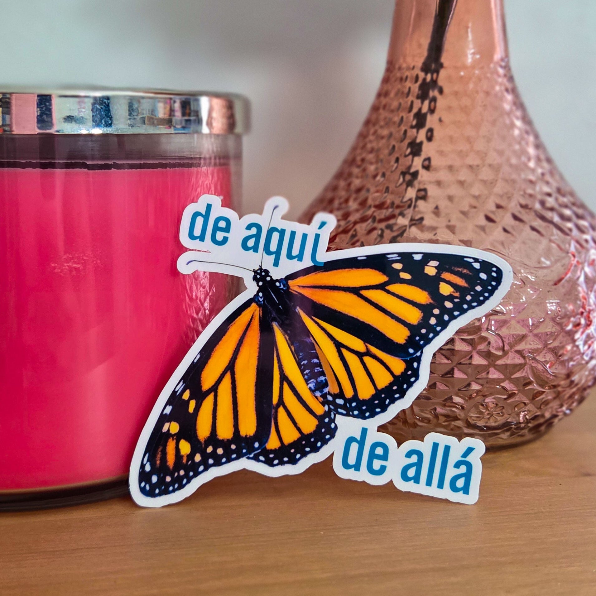 Pink candle, vase with peach rose, and butterfly sticker on a wooden surface