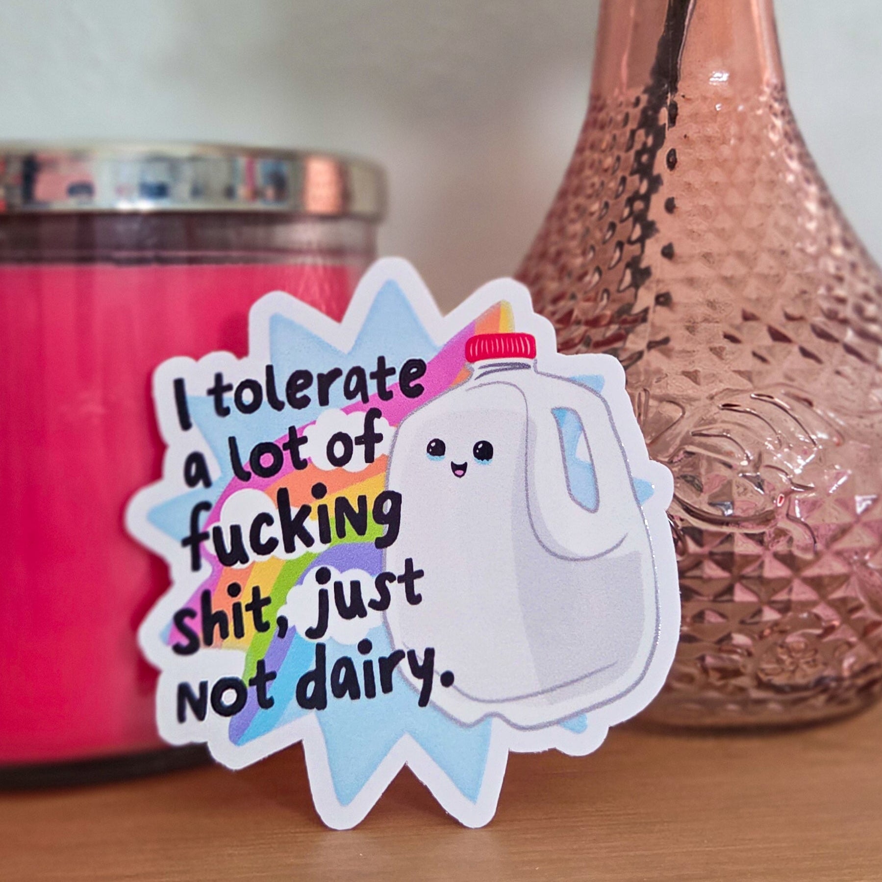 Sticker with text on a surface with a pink candle and vase in the background