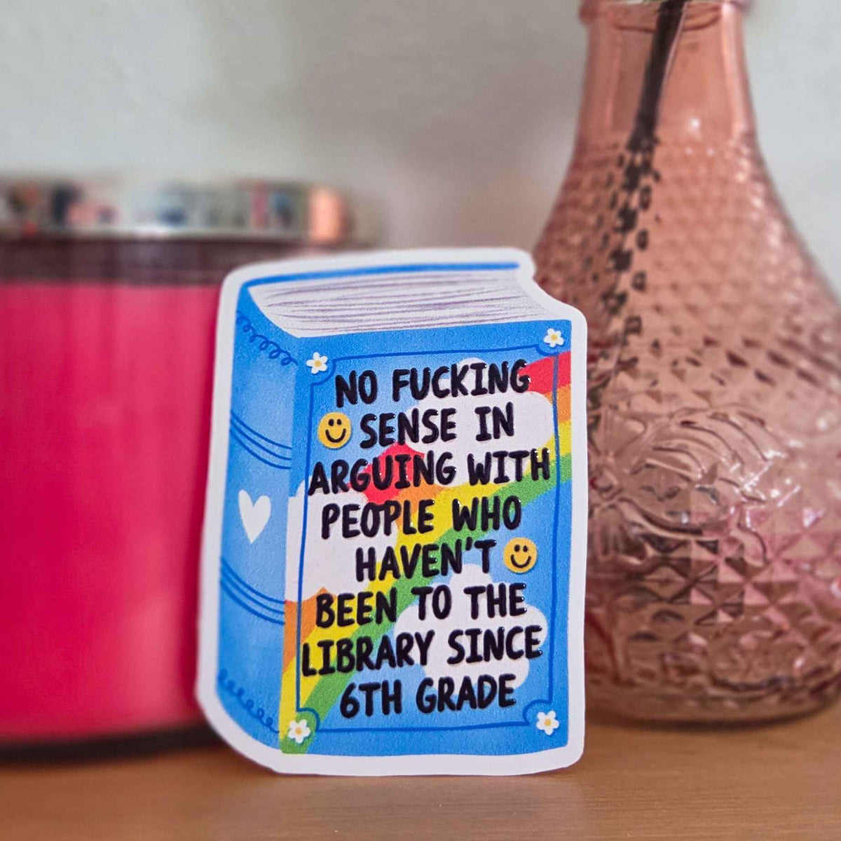 Book-shaped sticker with humorous text on a surface with a vase and container in the background