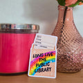Card with 'Long Live the Public Library' text next to a pink candle and vase with a rose on a wooden surface.