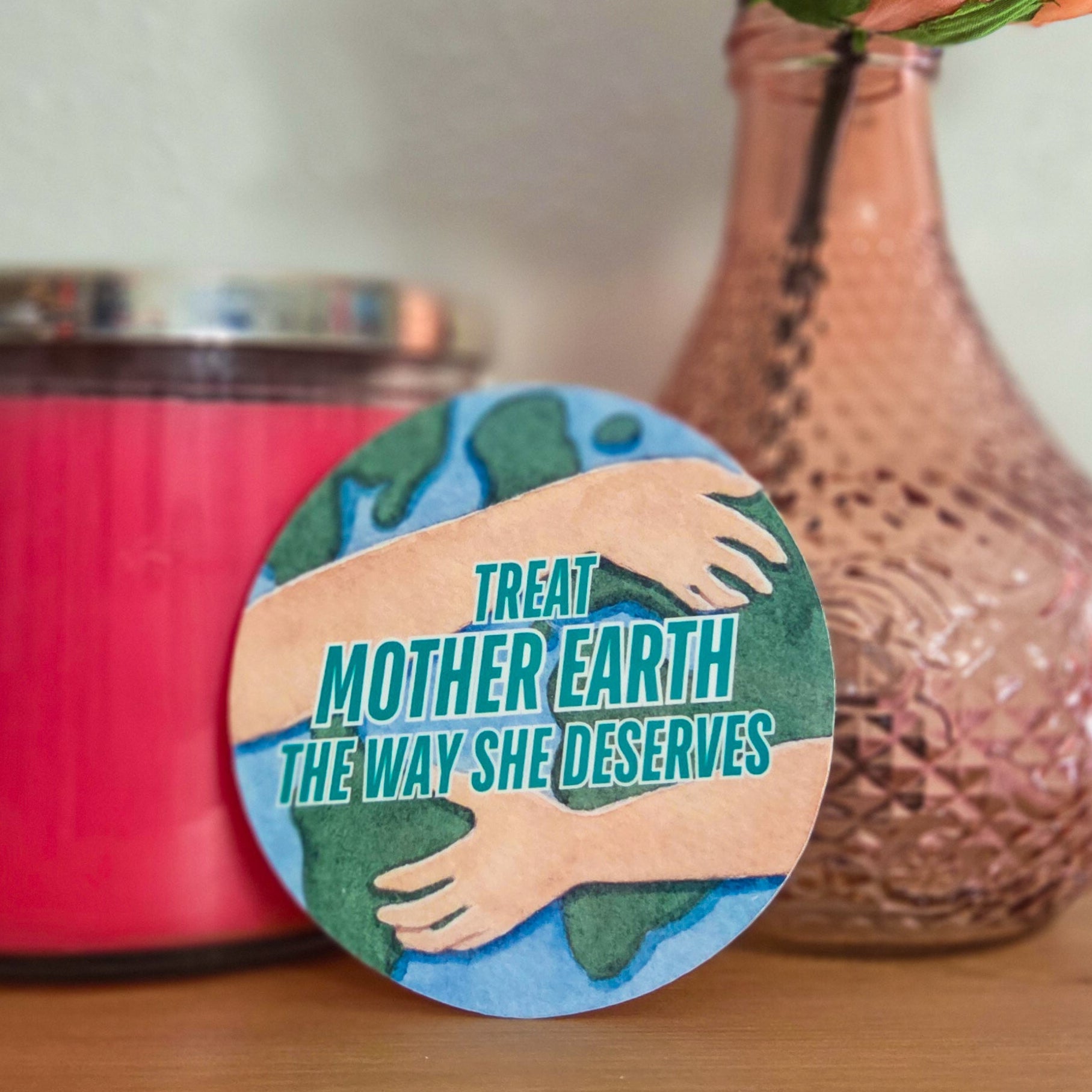 Circular sticker with 'Treat Mother Earth the way she deserves' text on a pink candle and vase with flowers.