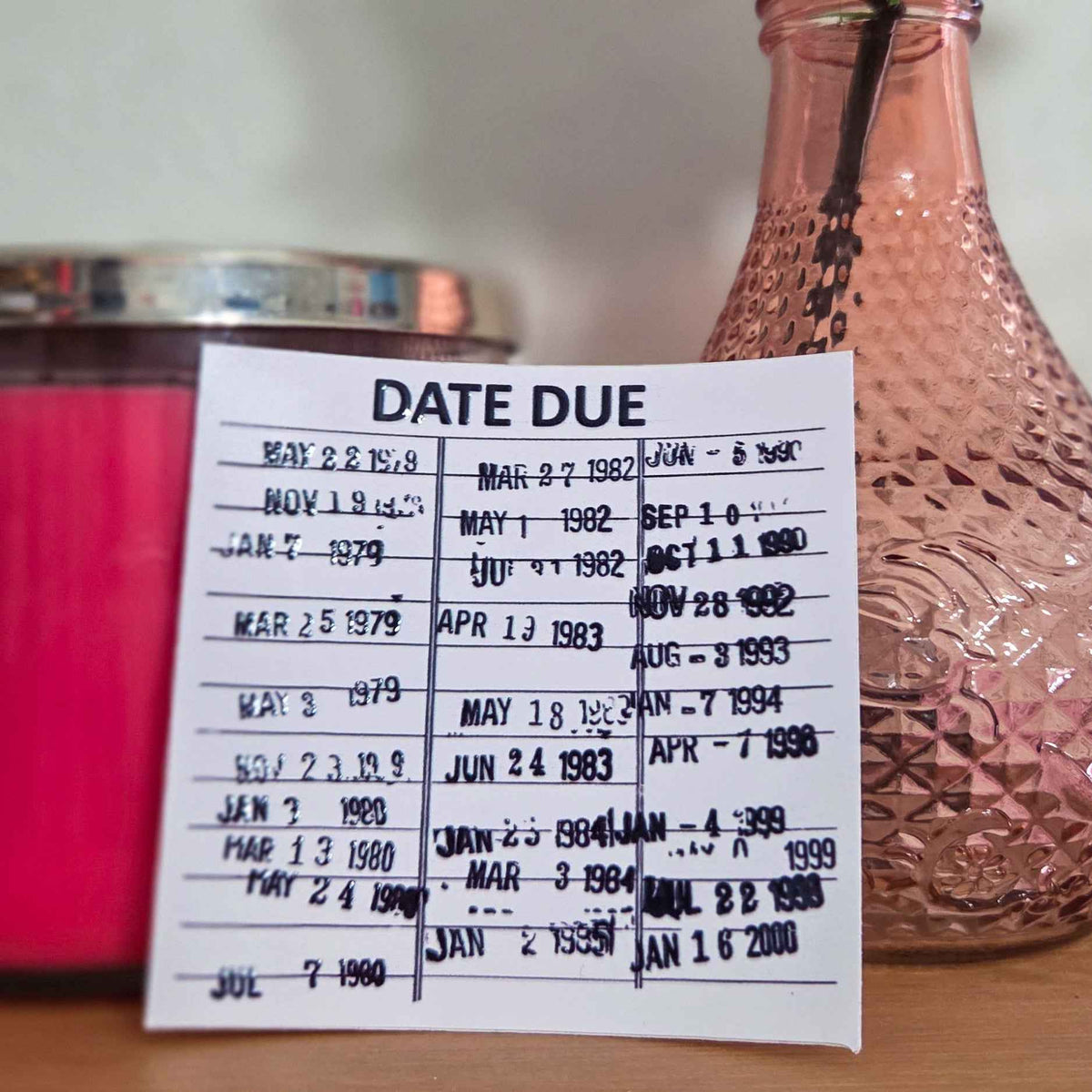 Sticker with  vintage library card 'DATE DUE' text on a wooden surface with a pink rose in a vase.