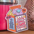 A die-cut sticker with a colorful design that reads ‘Self Love Juice' resting on a wooden surface.