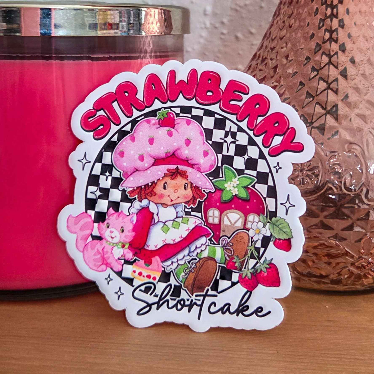 Sticker of Strawberry Shortcake with a pink candle and decorative item in the background