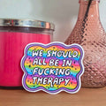 Sticker with colorful text on a surface with a pink candle and decorative vase.