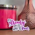 Pink candle and decorative vase with a rose on a wooden surface, accompanied by a motivational sticker.