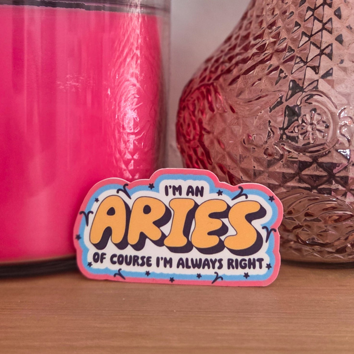 A die-cut sticker with a colorful astrological design that reads 'I'M A ARIES OF COURSE I’M ALWAYS RIGHT’  resting on a wooden surface.