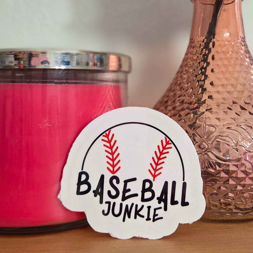 Pink candle and vase with a rose on a wooden surface, featuring a 'Baseball Junkie' sticker.