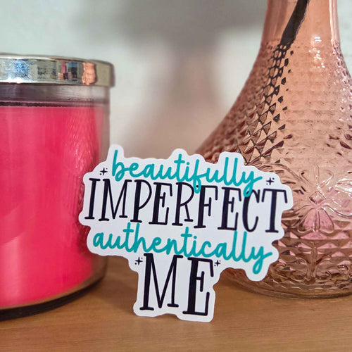 Sticker with 'beautifully imperfect authentically ME' text next to a pink candle and decorative vase.
