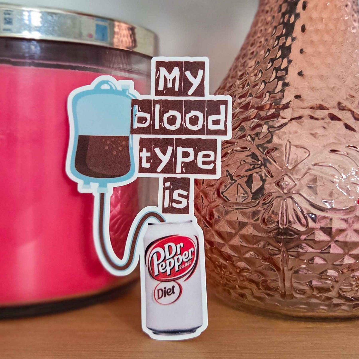 Sticker with 'My blood type is Diet Dr Pepper' text next to a pink candle and textured vase.