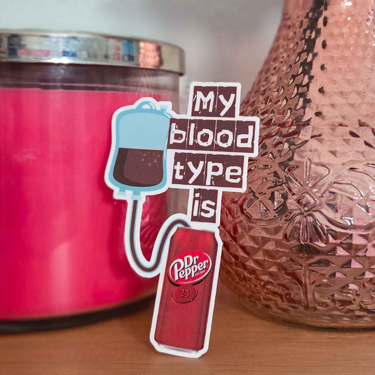 Sticker with 'My blood type is Dr Pepper' text next to a pink candle and textured vase.