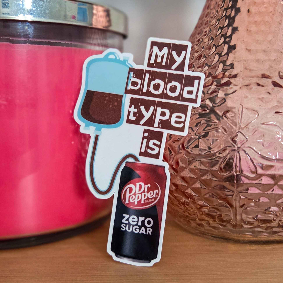Sticker with 'My blood type is Dr Pepper Zero Sugar' text next to a pink candle and textured vase.