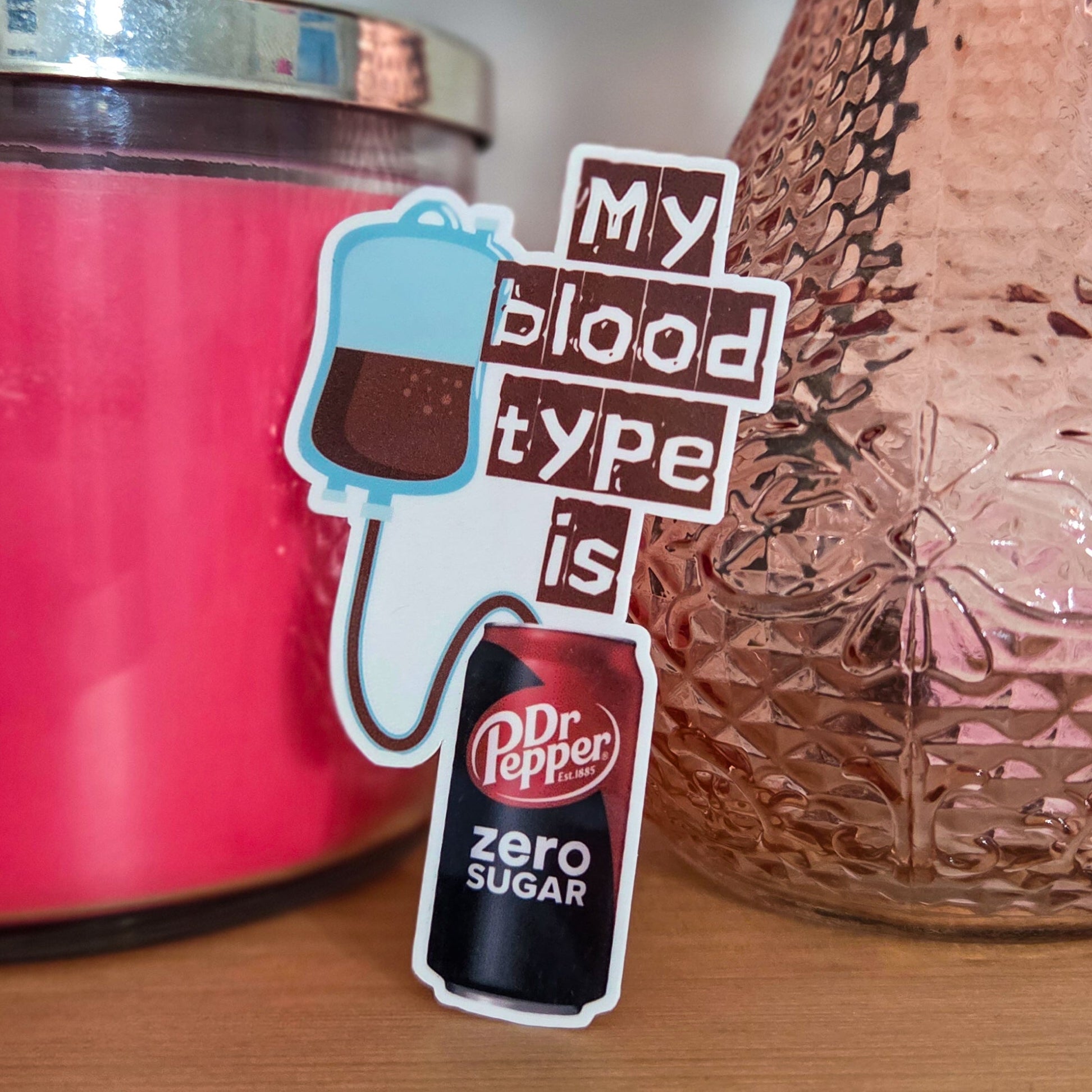 Pink candle and rose gold vase on a wooden surface with a 'My blood type is Dr Pepper zero sugar' sticker.