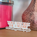 Pink textured vase with a pink candle and a decorative card on a wooden surface.