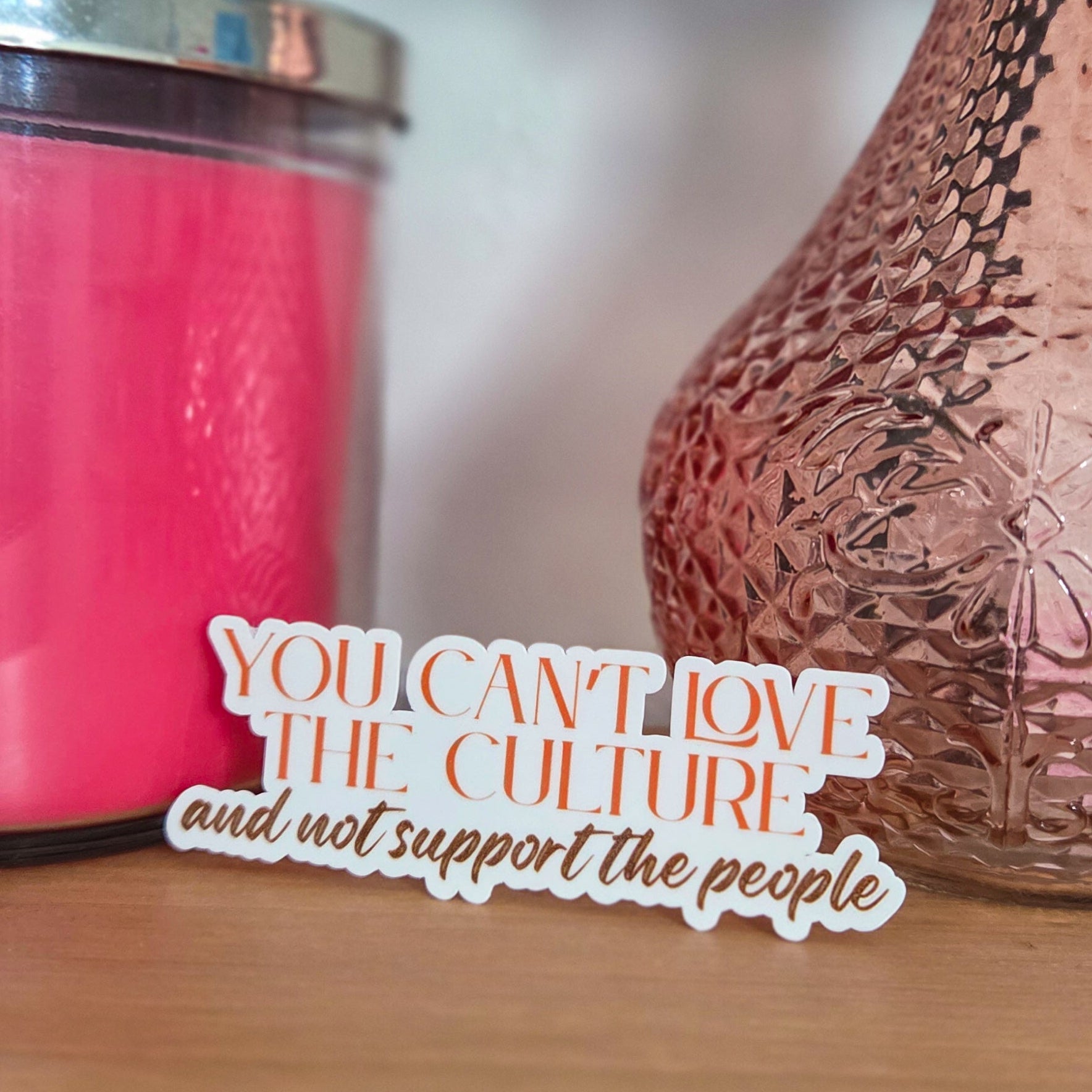 Pink textured vase with a pink candle and a decorative card on a wooden surface.