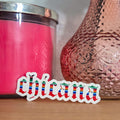 Pink candle and textured vase on a wooden surface with 'chicana' sticker.