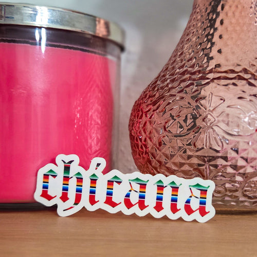 Pink candle and textured vase on a wooden surface with 'chicana' sticker.