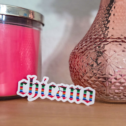 Pink textured vase and pink candle on a wooden surface with 'chicano' sticker.