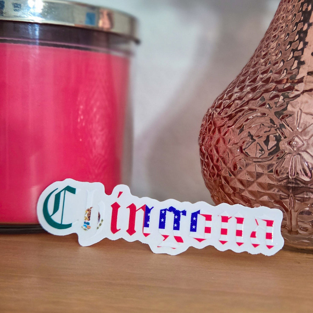 Pink candle and decorative vase on a wooden surface with a spanish sticker in the foreground.