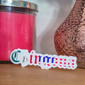 Pink candle and decorative vase on a wooden surface with a spanish sticker in the foreground.