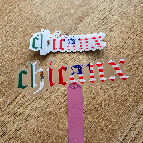 'chicanx' stickers with American flag and Mexican flag designs on a wooden surface.