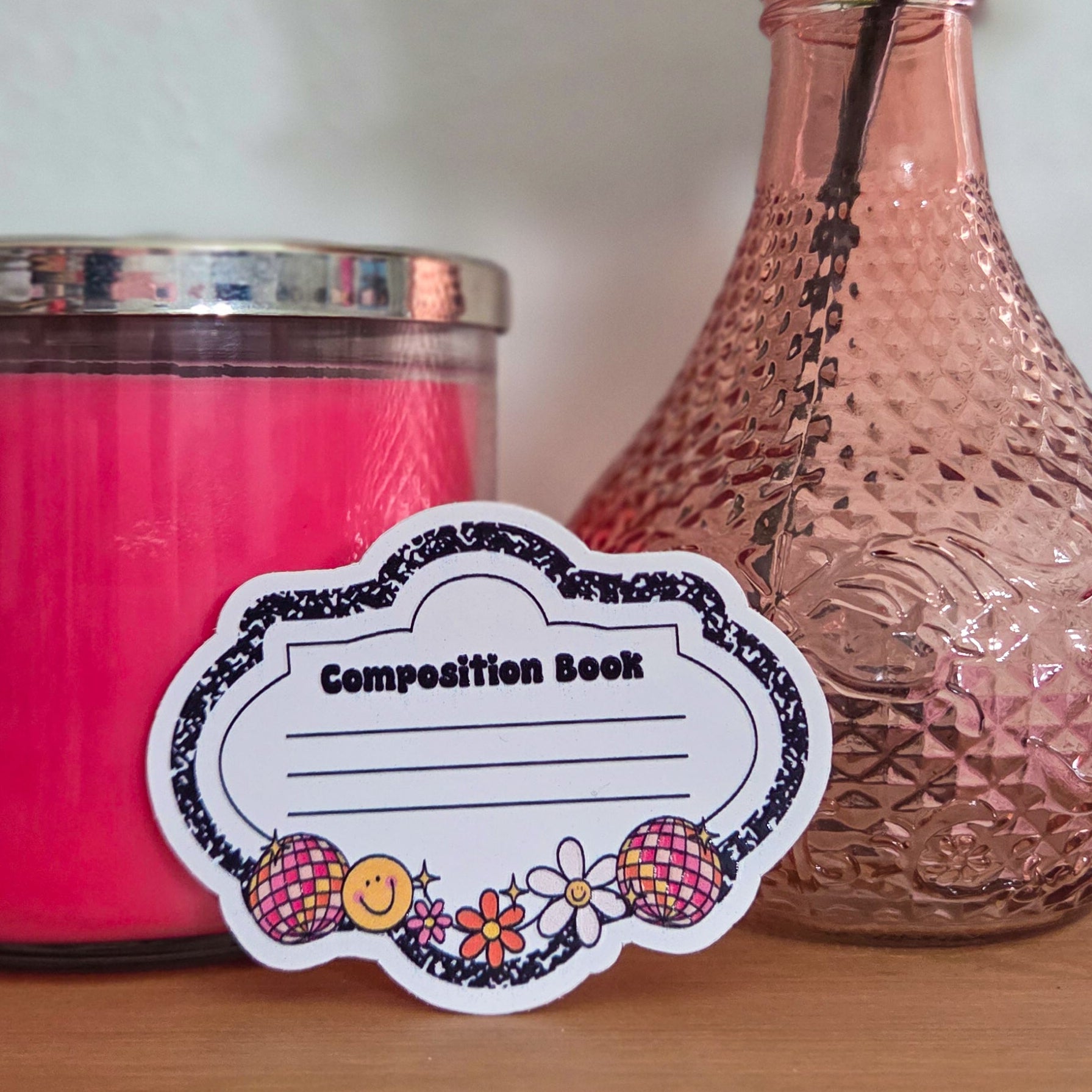 Pink candle and vase with a decorative label on a wooden surface