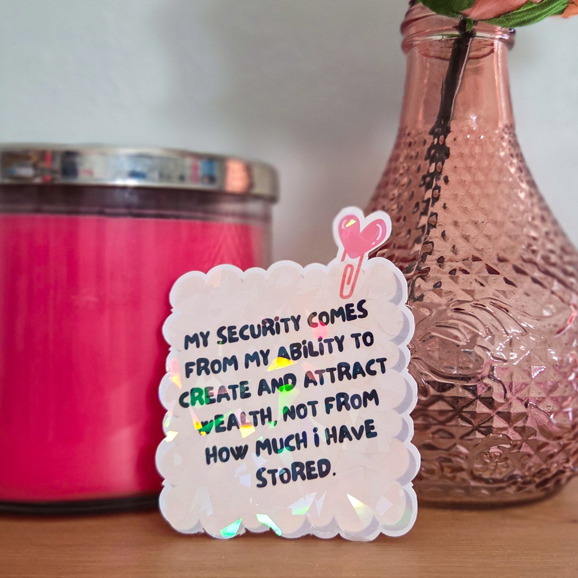 Decorative sticker with motivational quote next to a pink rose in a vase on a wooden surface.