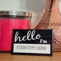 Candle, vase with a rose, and 'hello I'm attached to my e-reader' sticker on a wooden surface.