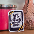 Decorative sticker with text next to a pink candle and vase with flowers on a wooden surface.