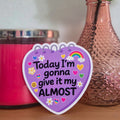 Pink candle, vase with peach roses, and motivational sticker on a wooden surface.