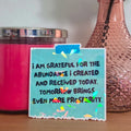 Pink candle, vase with a rose, and motivational sticker on a wooden surface.
