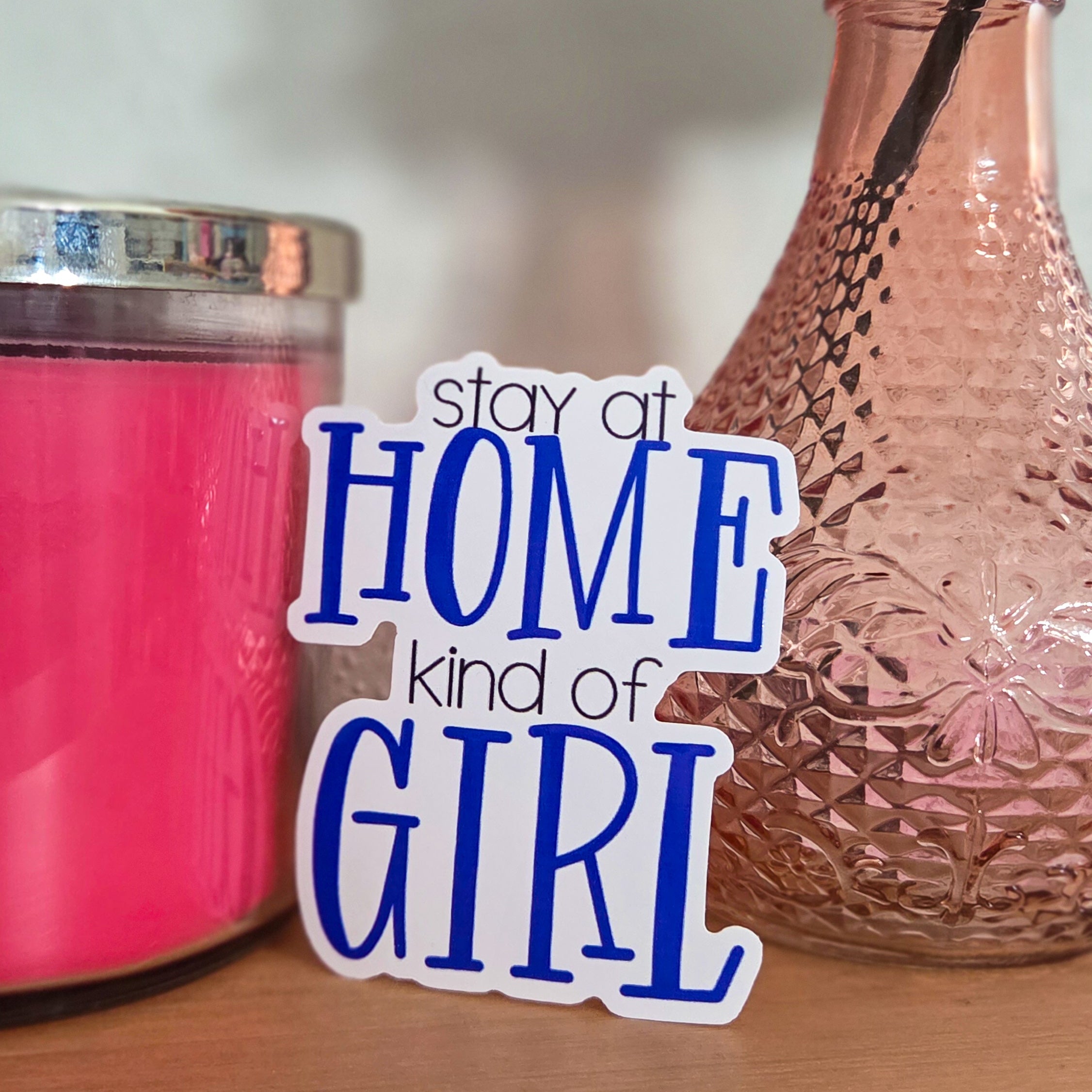 Pink candle and decorative vase with 'stay at home kind of girl' text on a wooden surface.