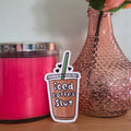 Pink candle, textured vase with a rose, and 'iced coffee slut' sticker on a wooden surface.