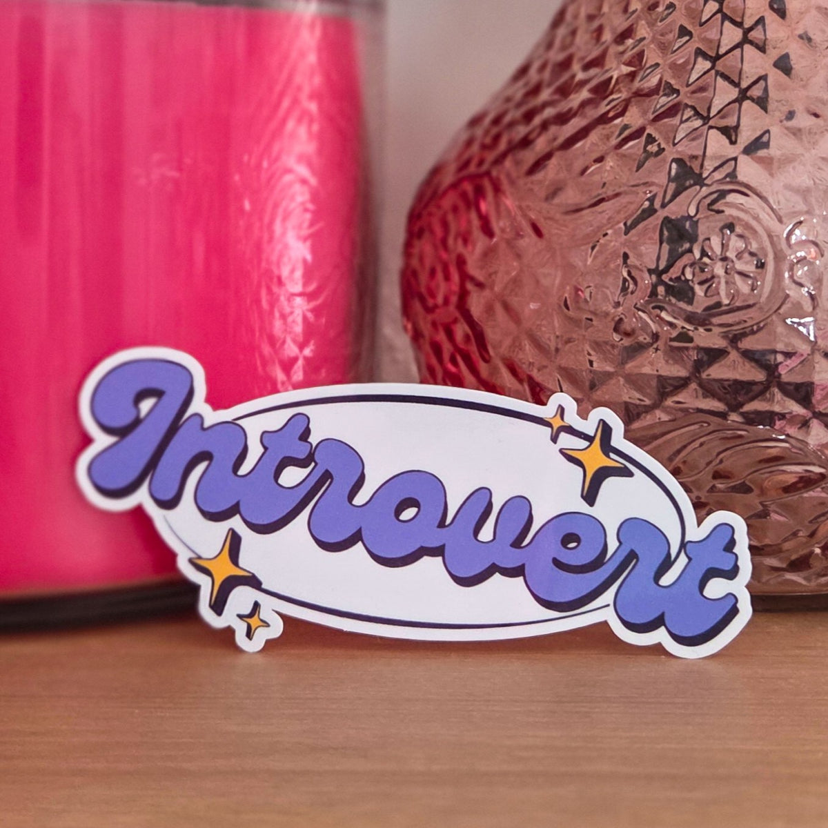A die-cut sticker that reads 'Introvert'  resting on a wooden surface.