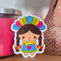 Sticker of a girl with braids and colorful headdress next to a pink vase with flowers on a wooden surface.