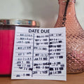 Sticker with 'DATE DUE' text on a wooden surface with a pink rose in a vase.