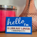 Blue card with 'hello I'm a library lover' text in front of a pink vase with a rose on a wooden surface.