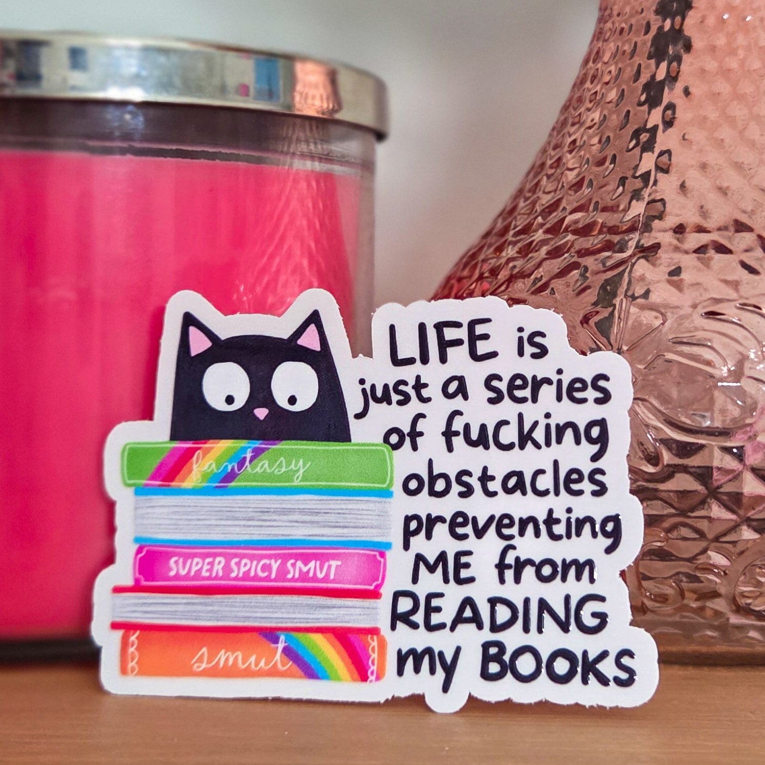 Sticker with text on a surface with a pink candle and vase in the background
