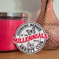 Pink candle and vase with peach rose on a wooden surface, featuring a sticker labeled 'Founding Member of the Millennials with Anxiety Club'.