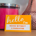 Yellow card with 'hello, I'm never without a narrator' text on a wooden surface with a pink candle and vase in the background.