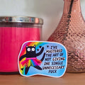 Pink candle, decorative vase with a flower, and colorful sticker on a wooden surface.