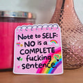 Pink notepad with motivational quote next to a vase with flowers and a candle.