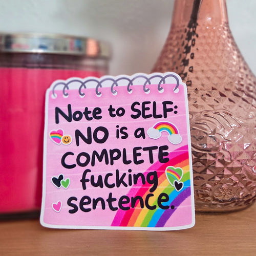 Pink notepad with motivational quote next to a vase with flowers and a candle.